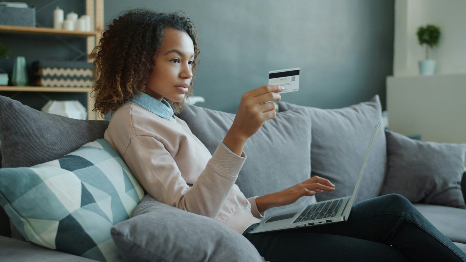 Someone on a sofa holding a card while buying something on a laptop