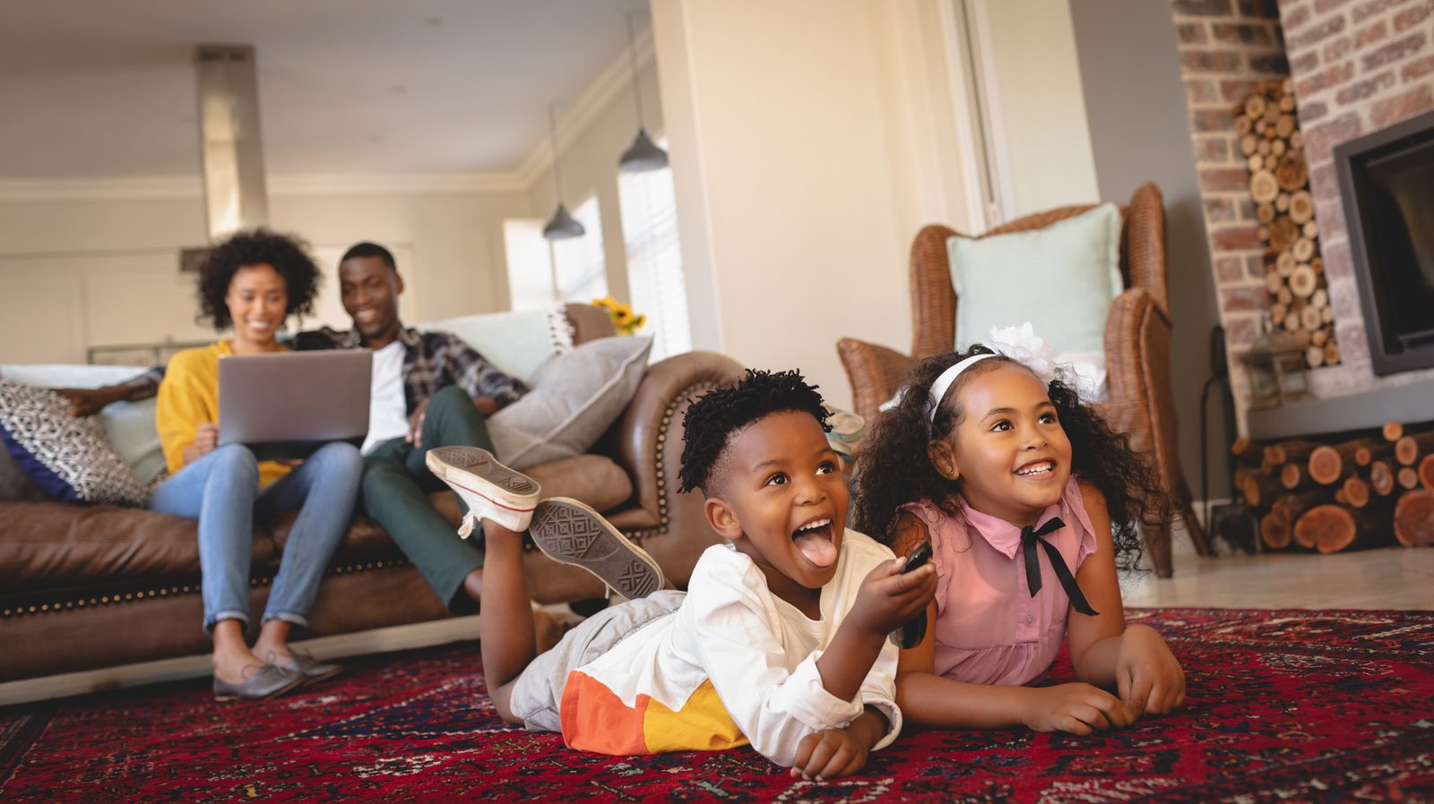 A family at home with the TV on while a laptop is open on the sofa